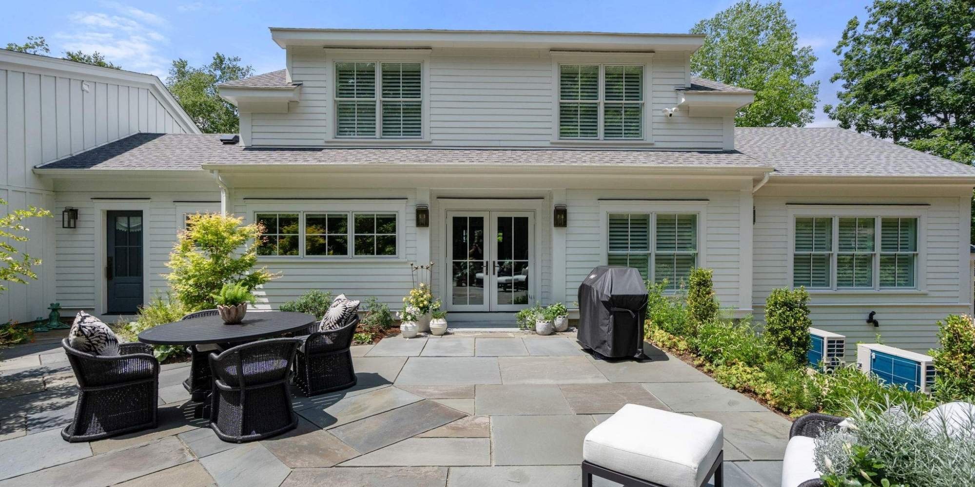 Exterior view from the back stone patio of a two-story custom home in Grafton, MA with French doors by Gilmore Building Co.