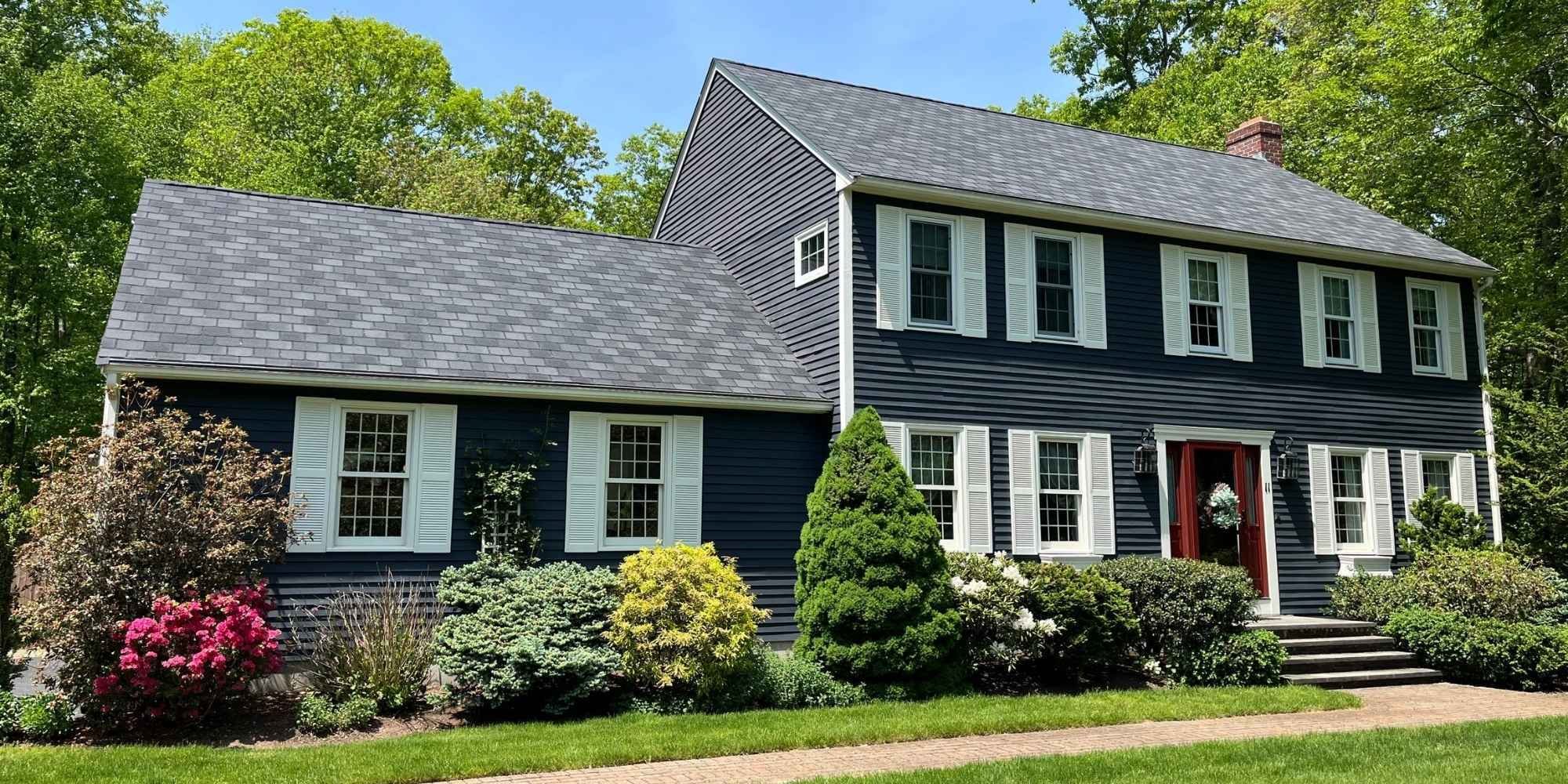 Exterior view of a home addition in Mendon, MA with navy blue siding and white shutters by Gilmore Building Co.