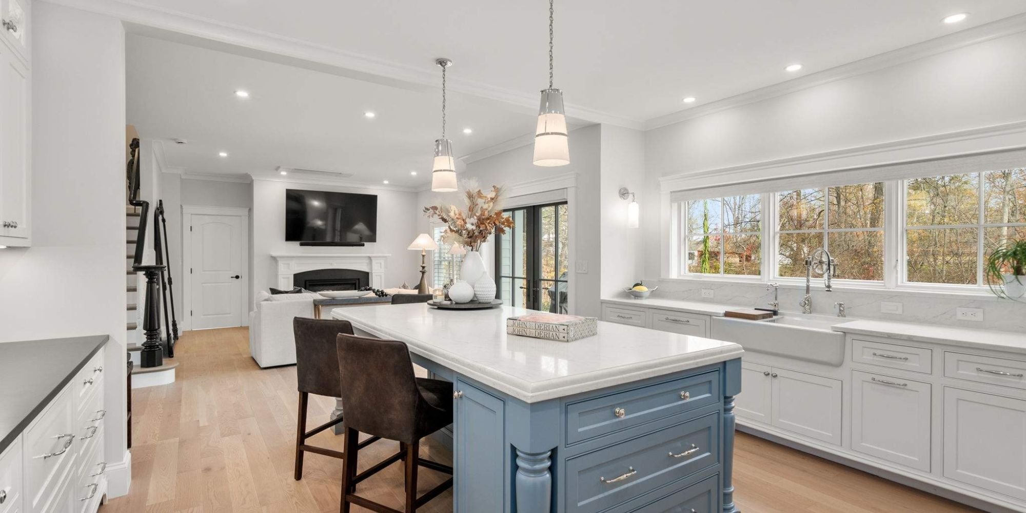 Kitchen inside a custom home featuring an island with seating and storage, custom lighting, and white cabinetry by Gilmore Building Co. in Grafton, MA