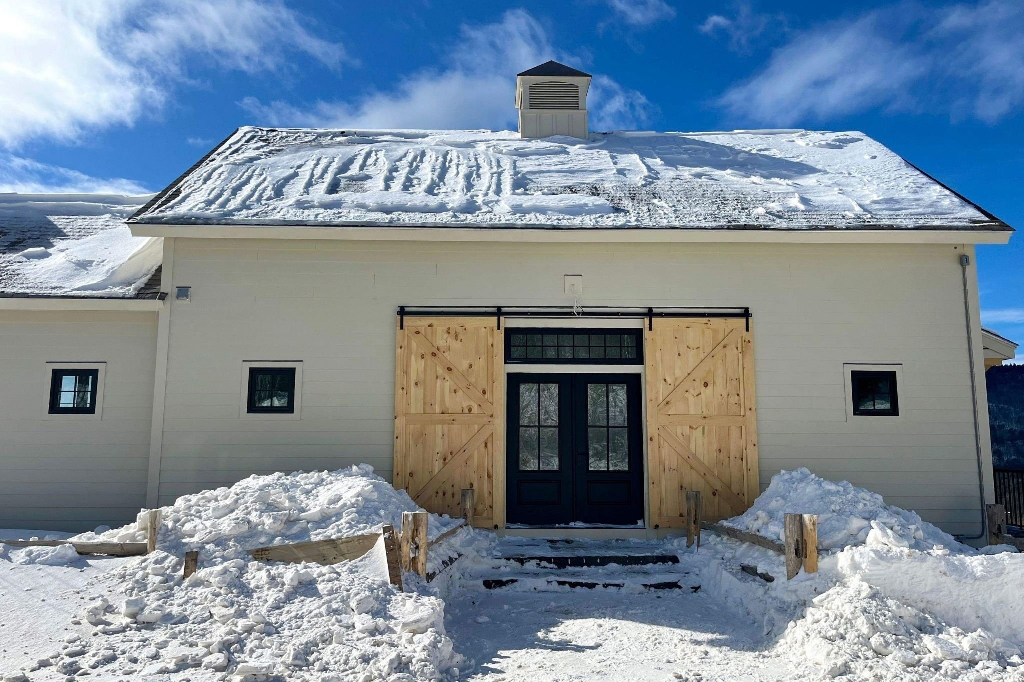 Exterior of a custom home in the snow featuring barn doors over French doors in Central Massachusetts by Gilmore Building Co