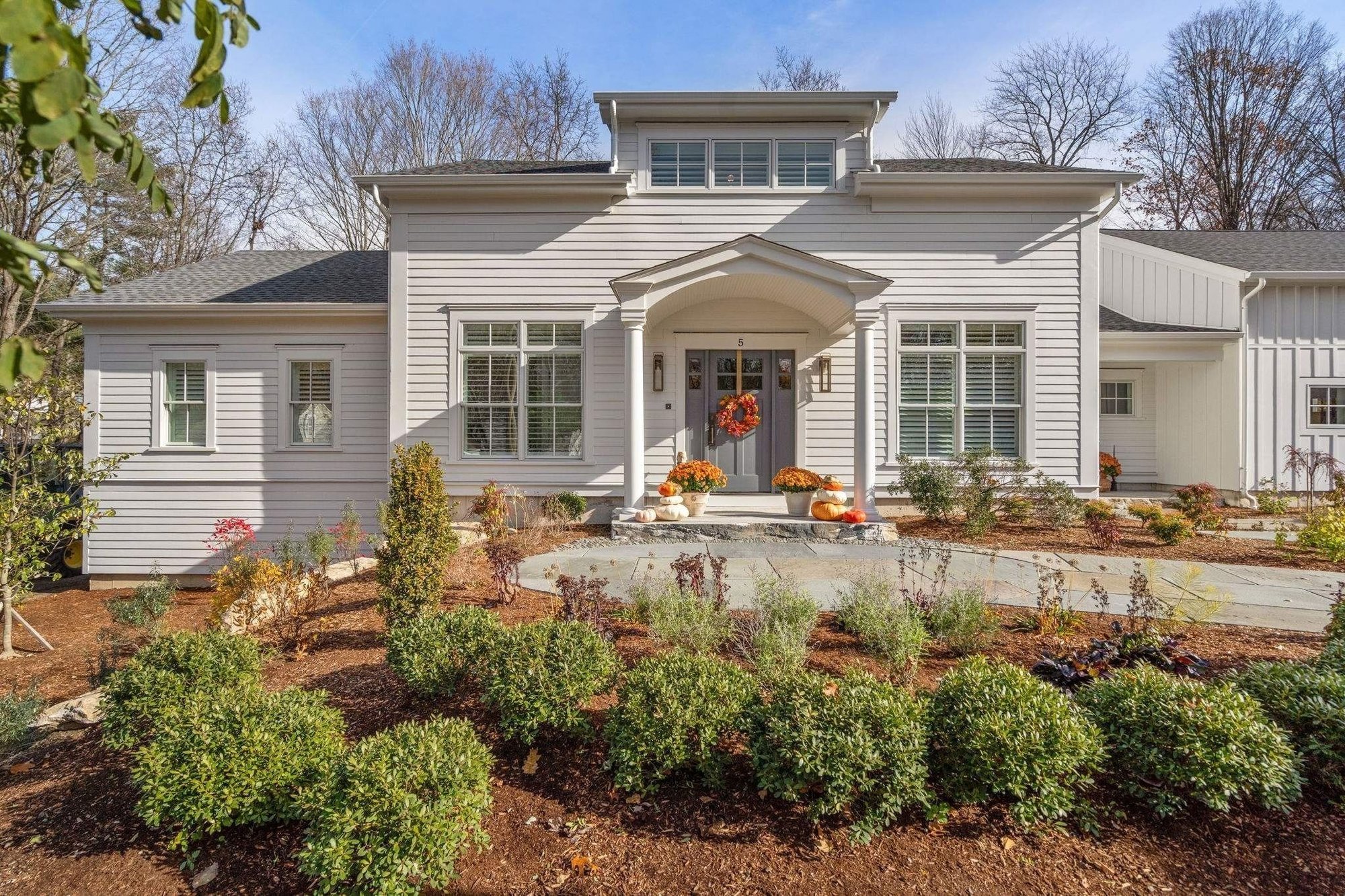 Front exterior of a custom home in Grafton, MA with a portico and landscaping by Gilmore Building Co