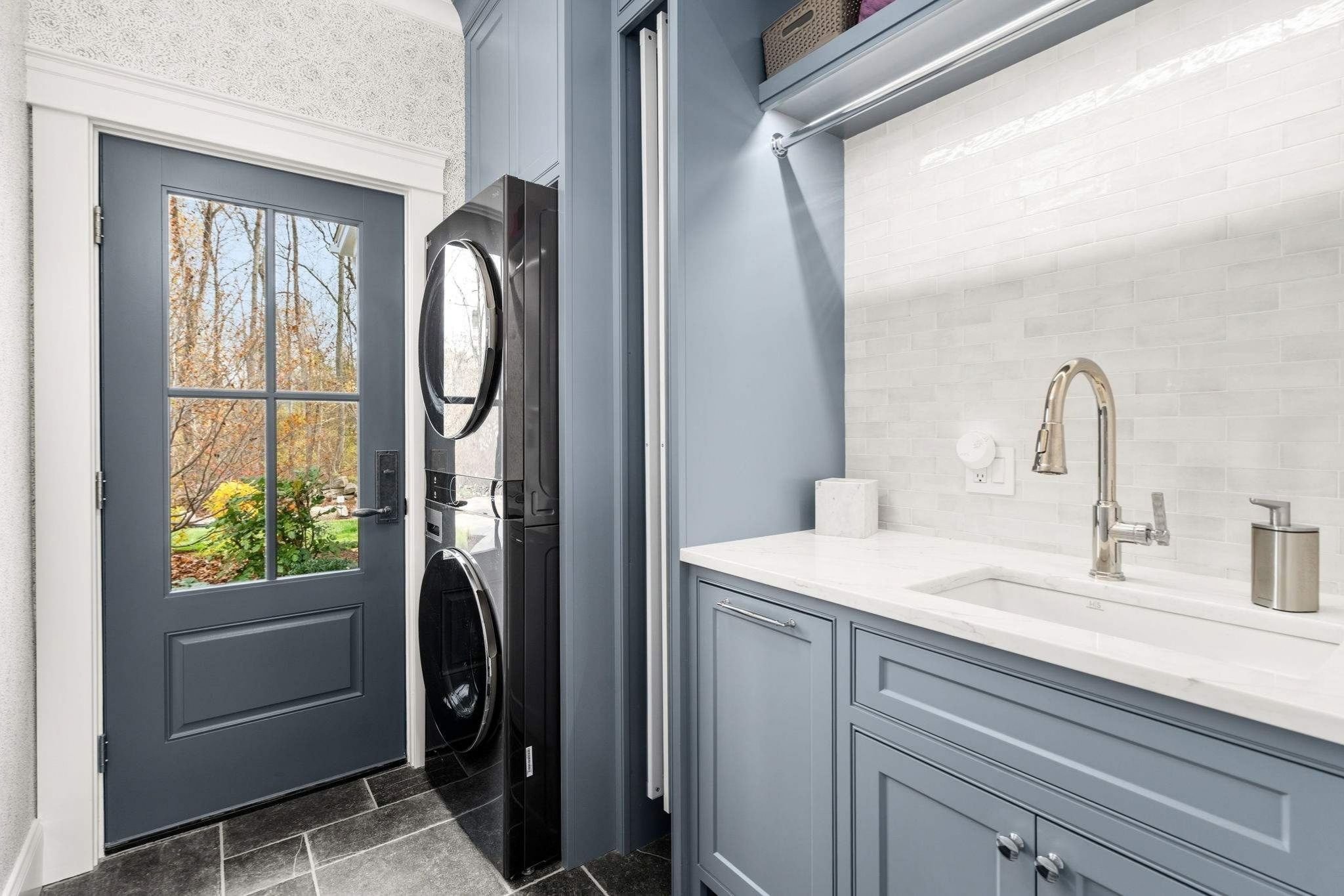 Laundry room in a custom home with stacked washer and dryer and a dedicated laundry sink by Gilmore Building Co. in Grafton, MA