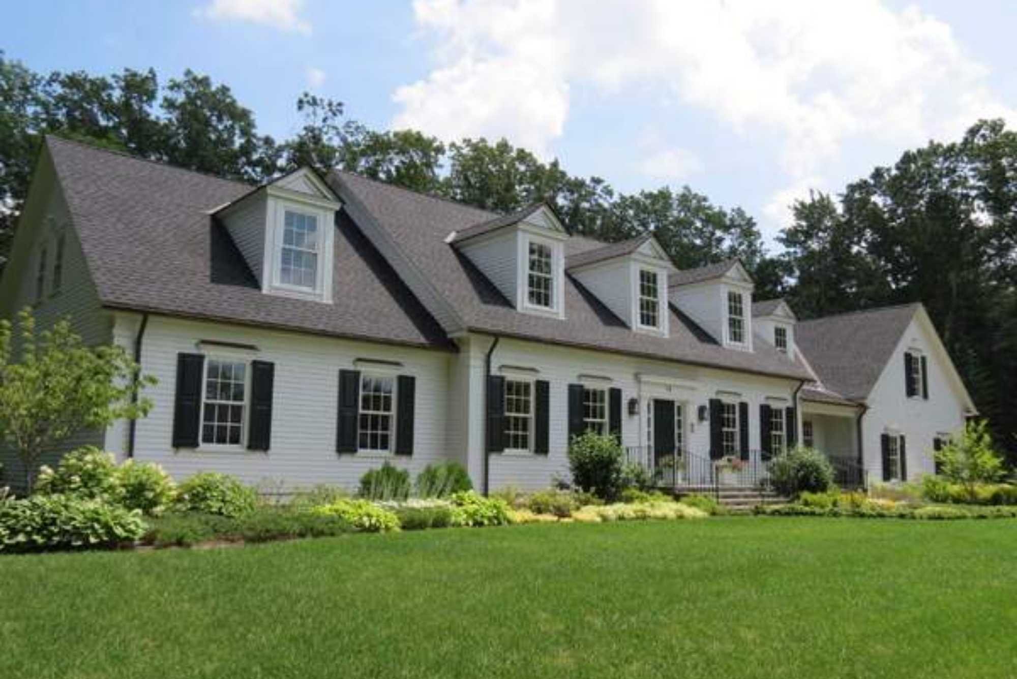 A custom home in Massachusetts with dormer windows, white siding, and black shutters by Gilmore Building Co.