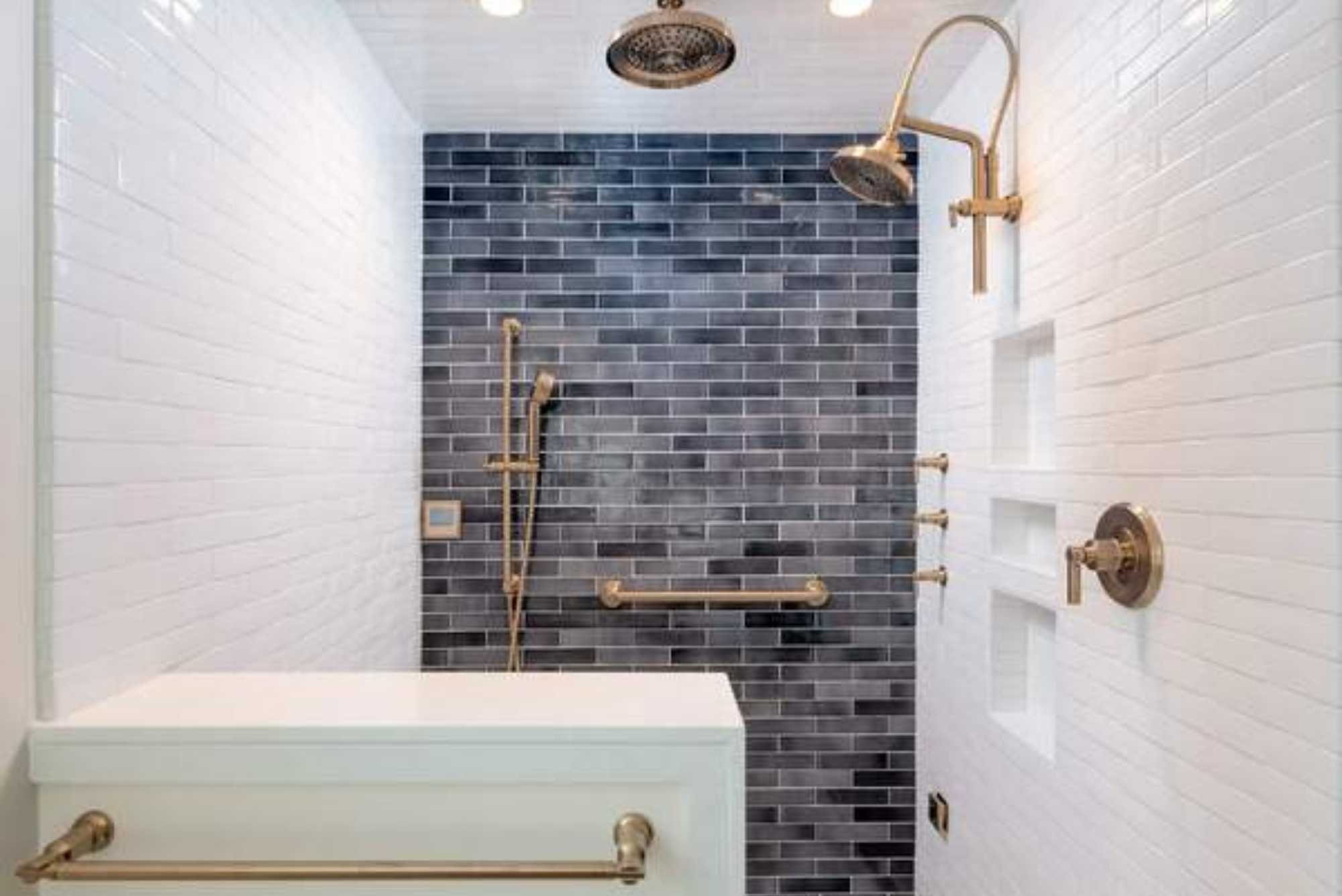 Custom no-entry shower remodel with brass hardware, two shower heads, white tile, and a statement wall of varied dark blue tile by Gilmore Building Co.