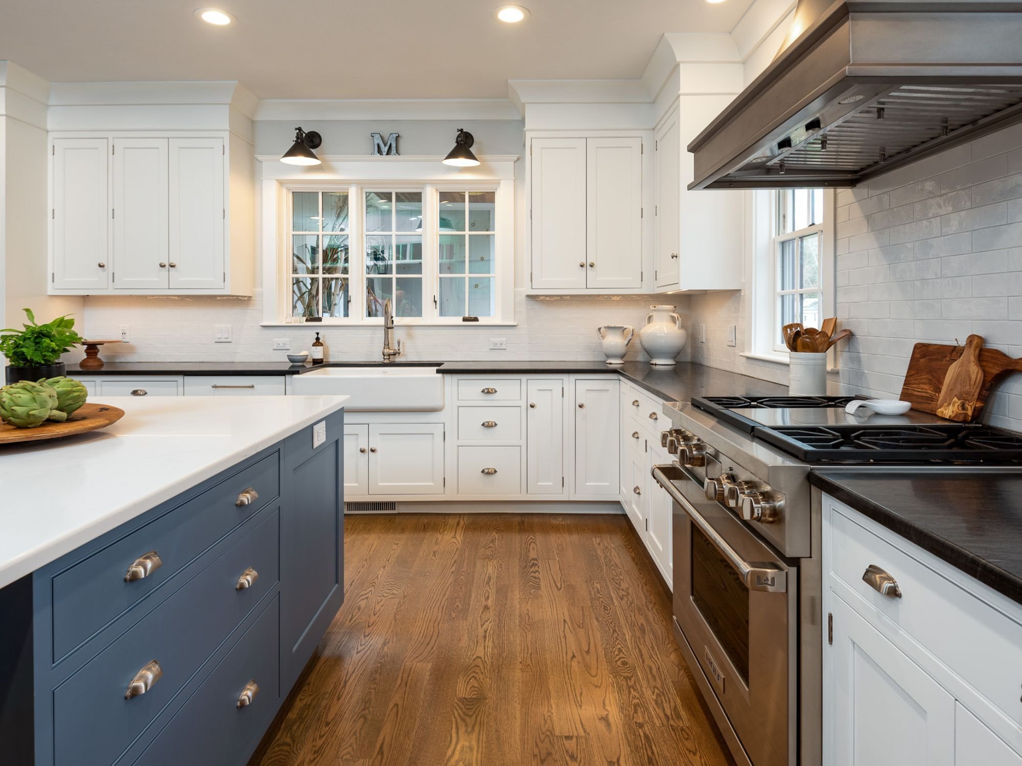 Custom kitchen remodel in Newton, MA with white cabinetry, a navy blue island, and a gas stove by Gilmore Building Co.