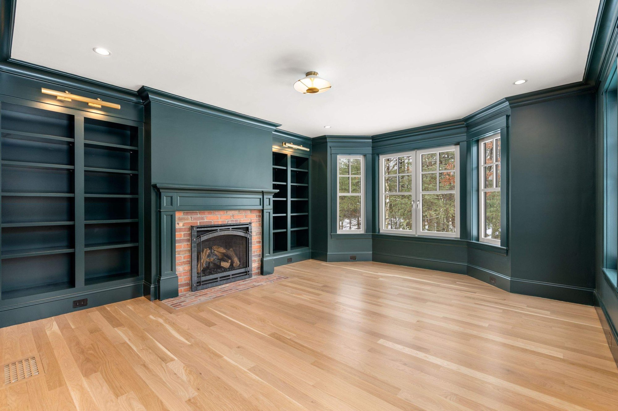 A remodeled living area with a fireplace, dark walls and trim, built-in bookshelves, and hardwood floors by Gilmore Building Co.