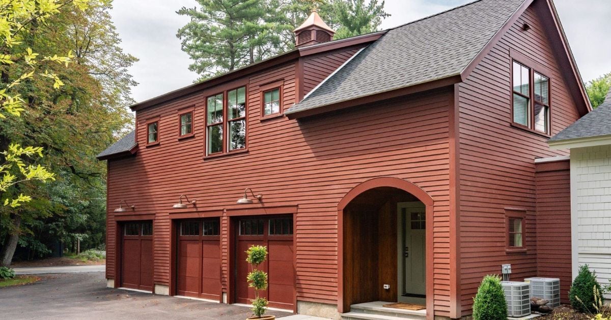 Attached ADU with living space above and a three-car garage below with red siding and an arched entryway by Gilmore Building Co.