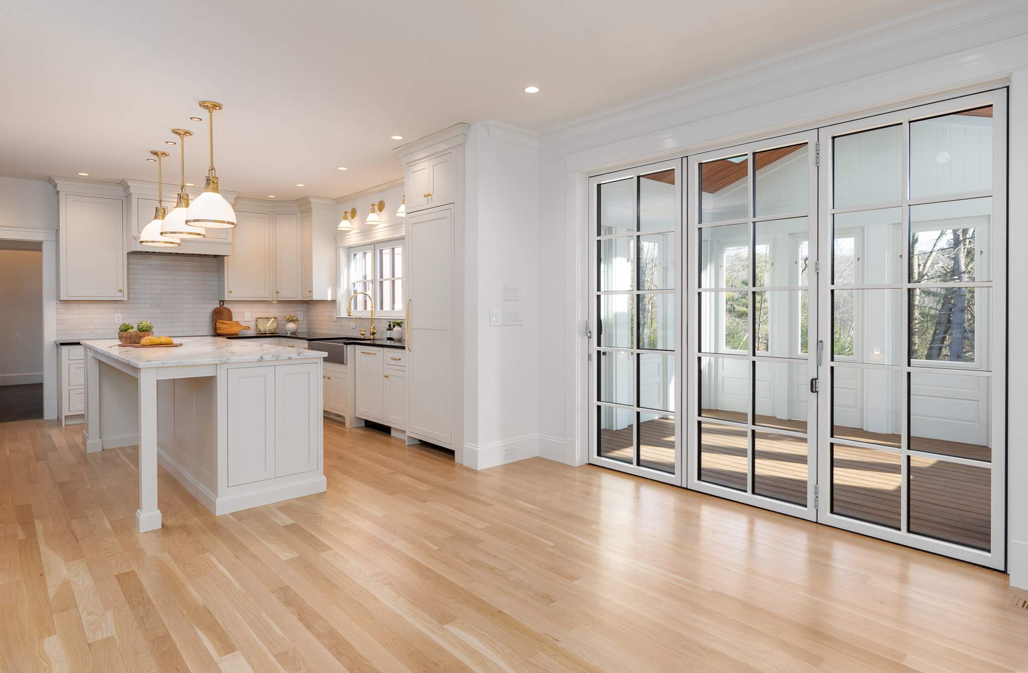 A remodeled kitchen with white cabinets, an island, a folding glass door that opens onto a sun porch by Gilmore Building Co.
